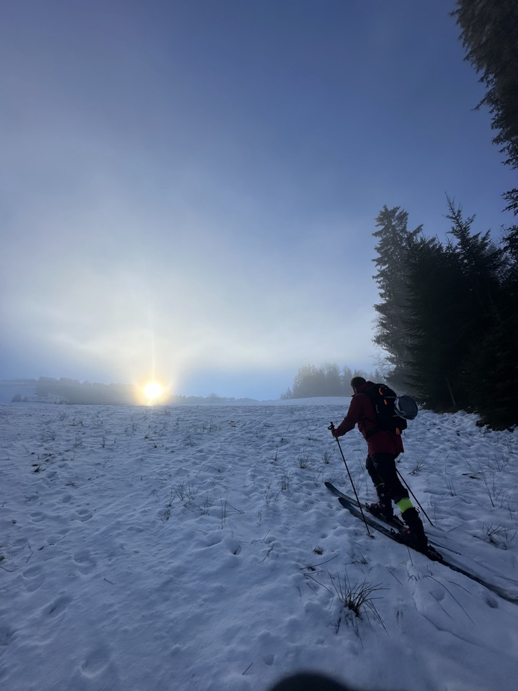 Ski touring towards a low sun across open snow at first light